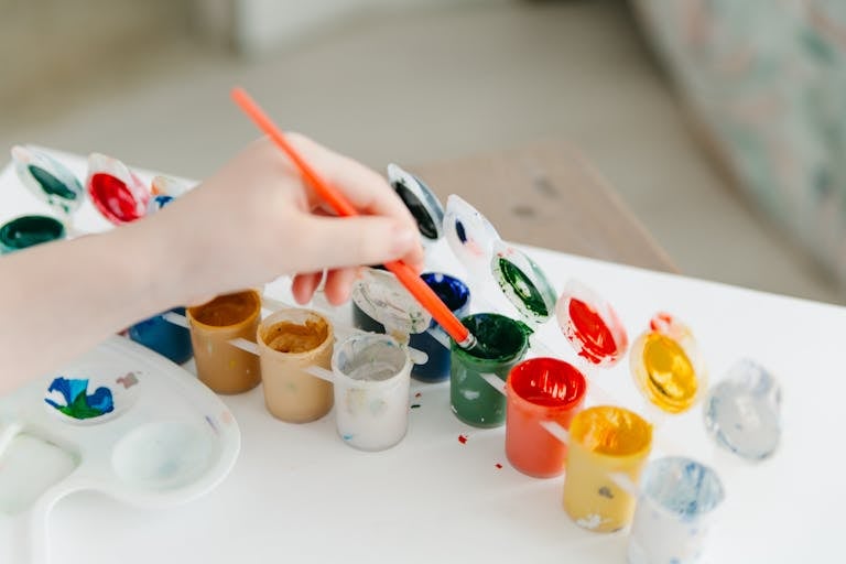 A child paints using a colorful watercolor palette, fostering creativity and fun.