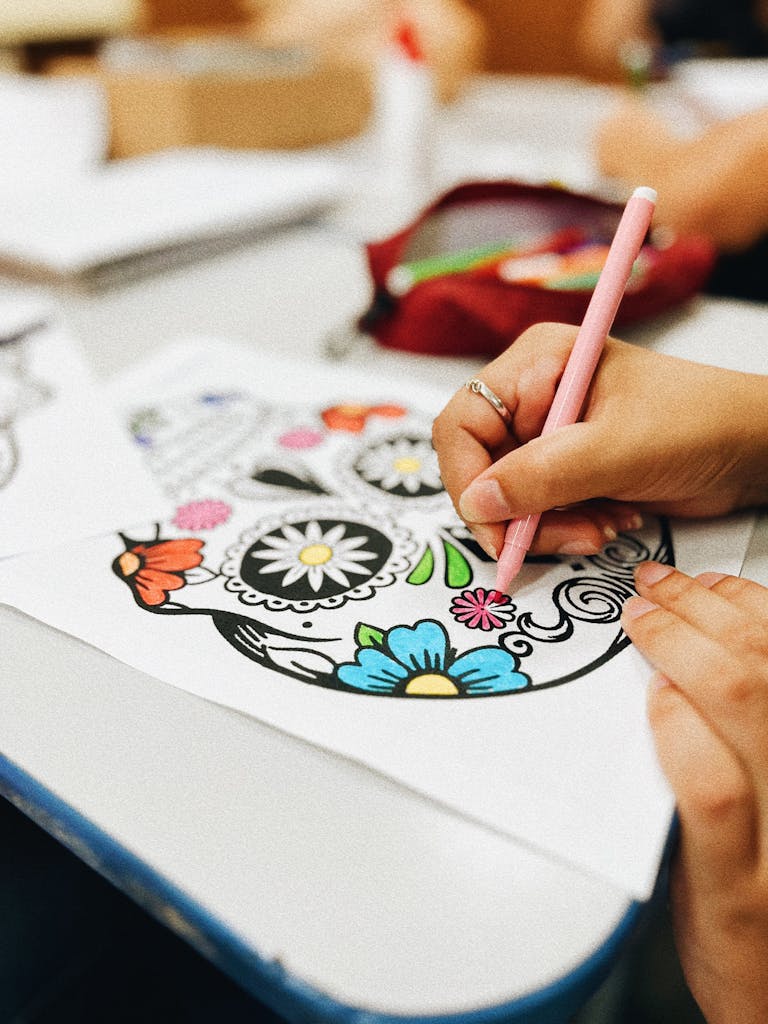 Close-up of hands coloring vibrant skull design in a classroom setting.