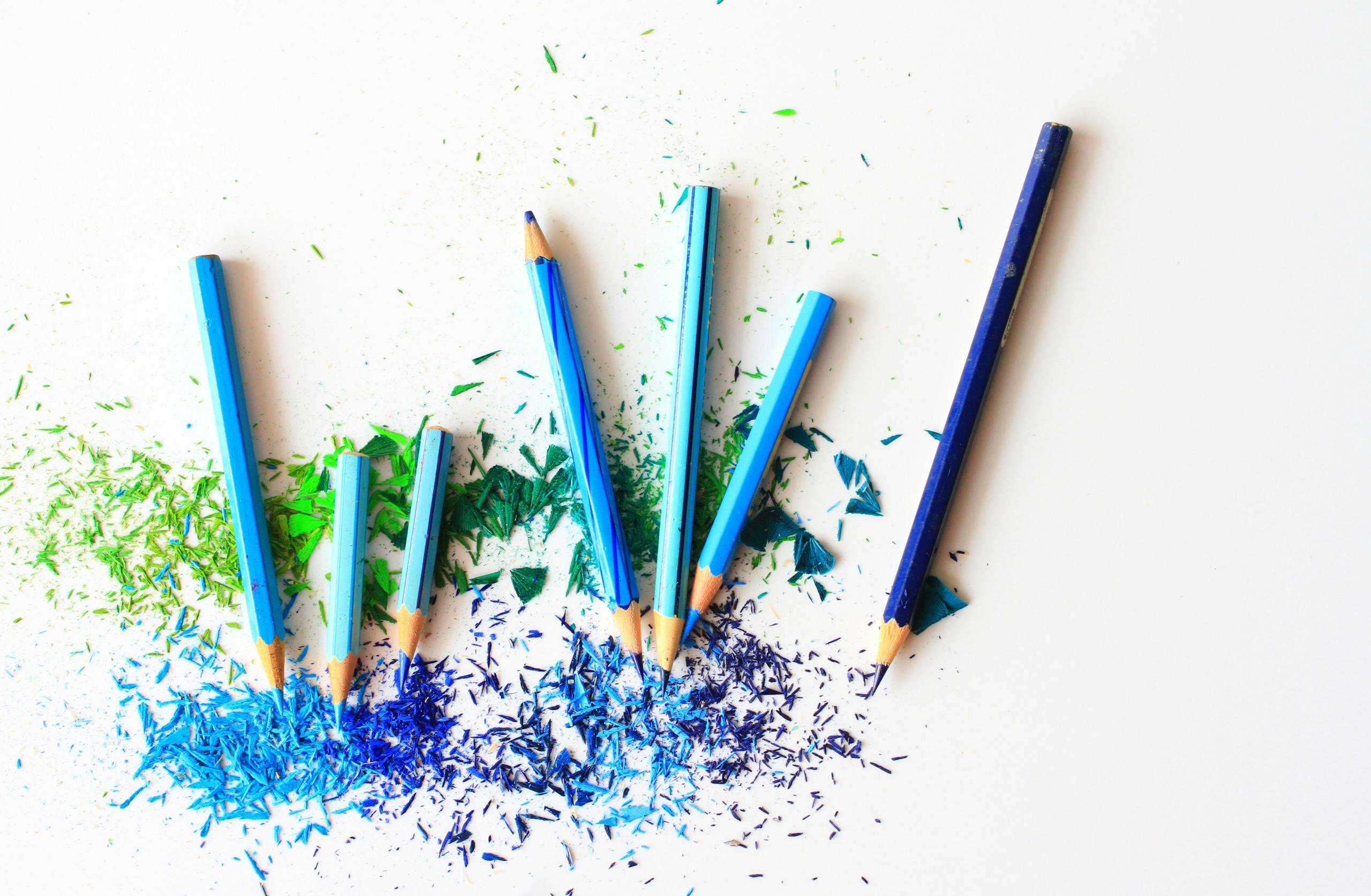 Creative display of colored pencils and vibrant shavings on a white background.